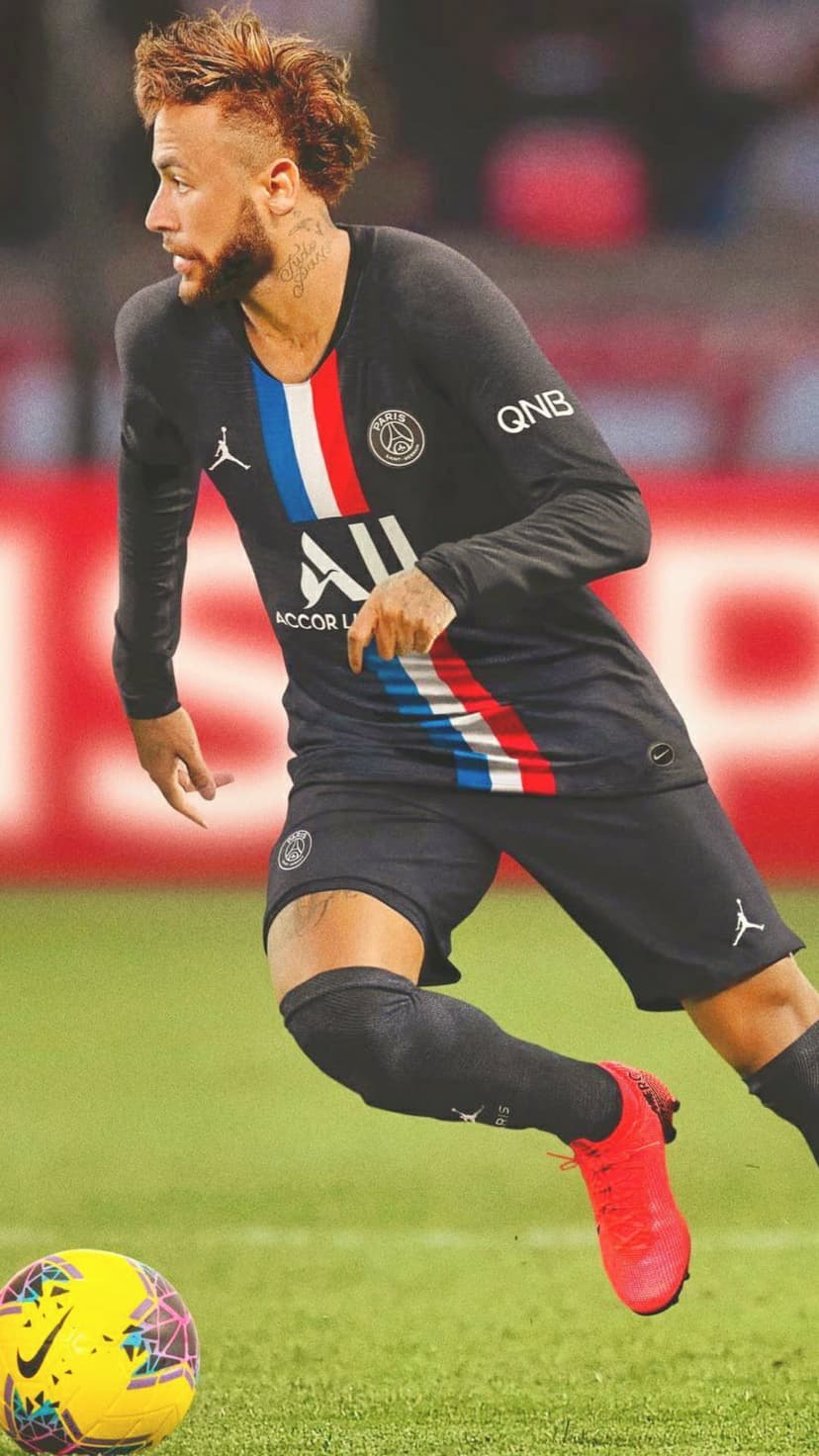 Neymar Jr dribbles a yellow football in a navy PSG jersey and red boots across a green grass field during a match.
