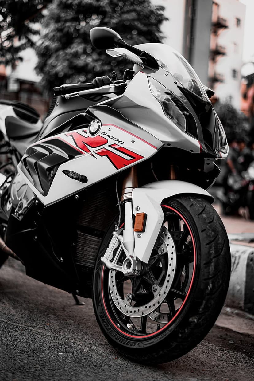 BMW S1000RR front wheel featuring a drilled brake disc, red rim pinstripe, and black tire on urban pavement.