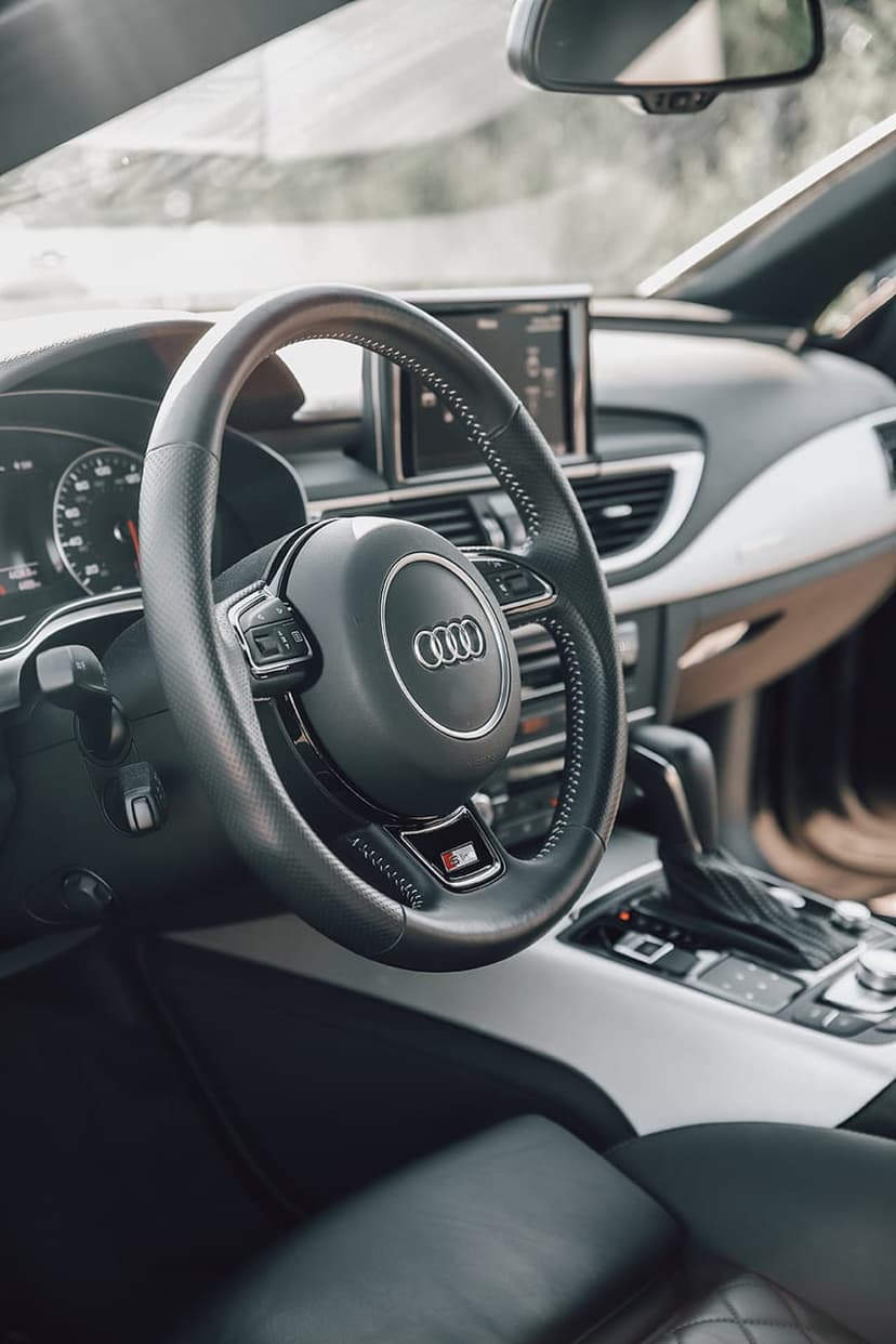 Audi S-line steering wheel with leather trim and silver logo inside a dark, modern car cabin with lit dashboard.
