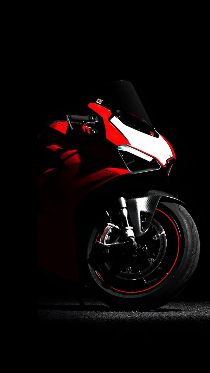 Red Ducati motorcycle front view with glowing headlights and rim accents against a pitch-black studio background.