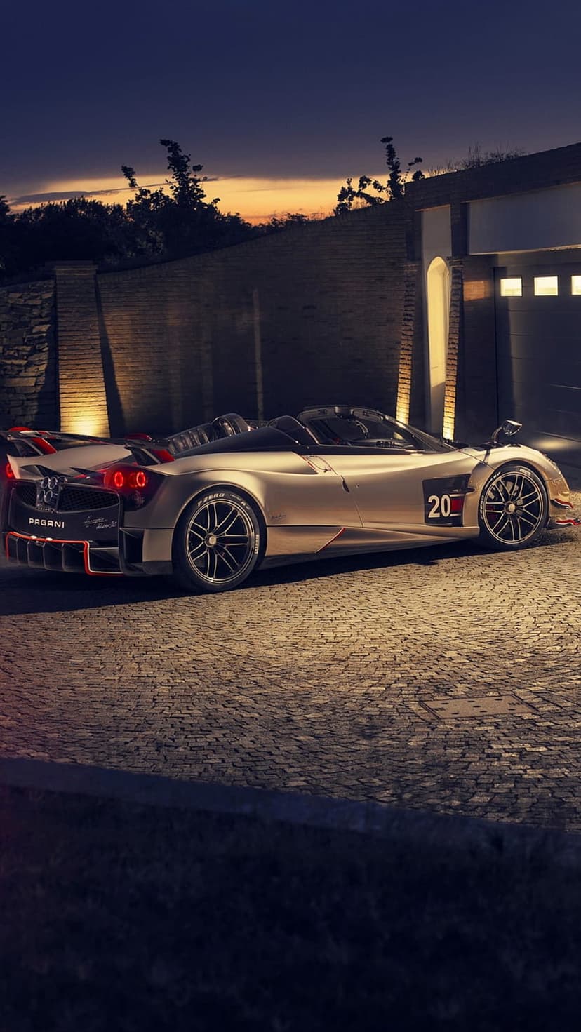 Pagani Huayra Roadster BC in golden bronze parked on a cobblestone driveway at twilight in front of a modern villa.