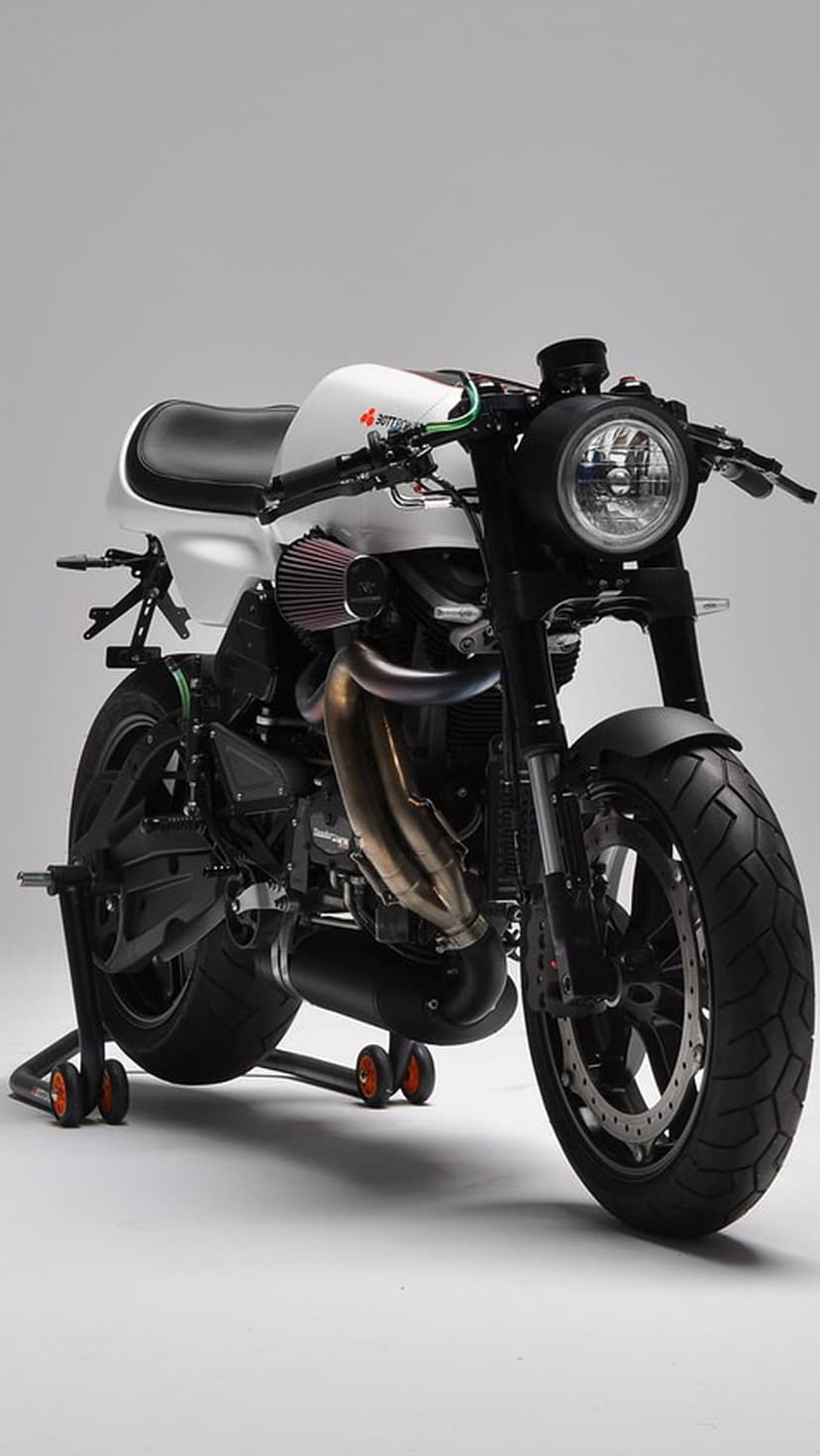 Custom white cafe racer motorcycle on a black stand featuring a red air filter and polished chrome exhaust pipe.