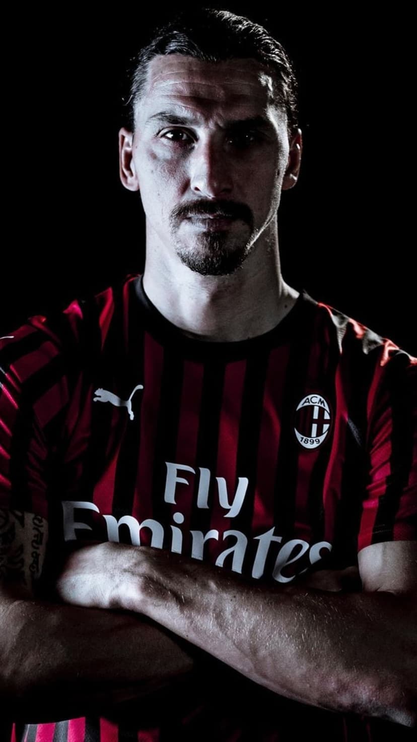 Zlatan Ibrahimovic with arms crossed wearing a red and black AC Milan jersey under cinematic studio lighting.