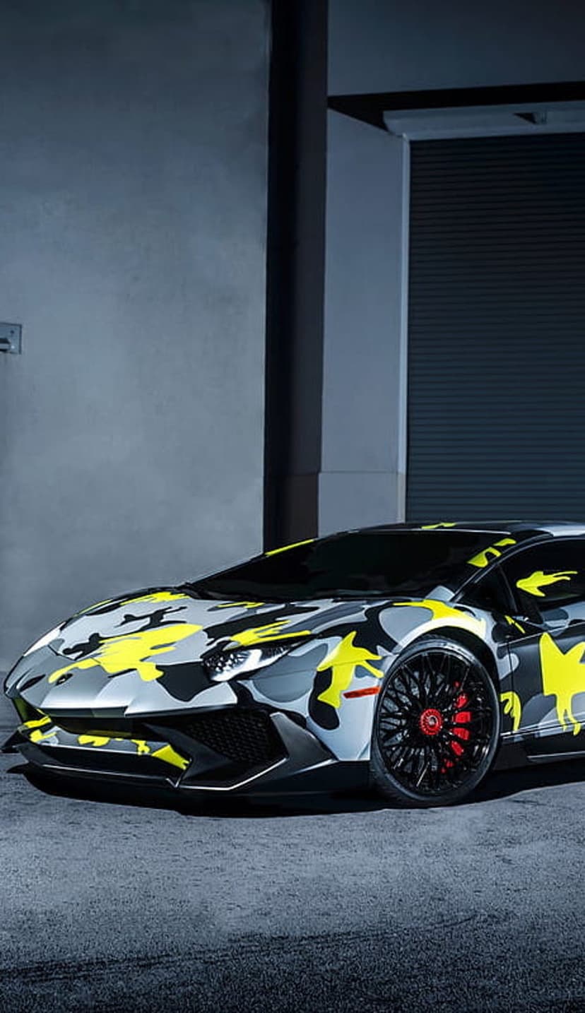 Lamborghini Aventador with yellow and gray camo wrap parked in a garage featuring red brake calipers.