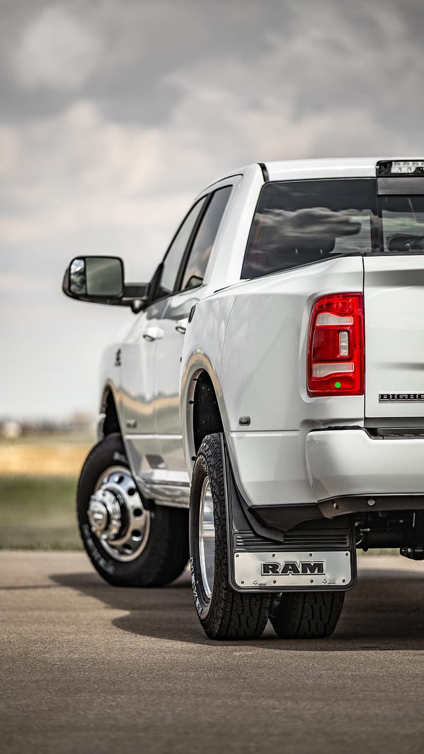 White Ram Heavy Duty truck rear view featuring dual wheels, branded mud flaps, and a red taillight under clouds.