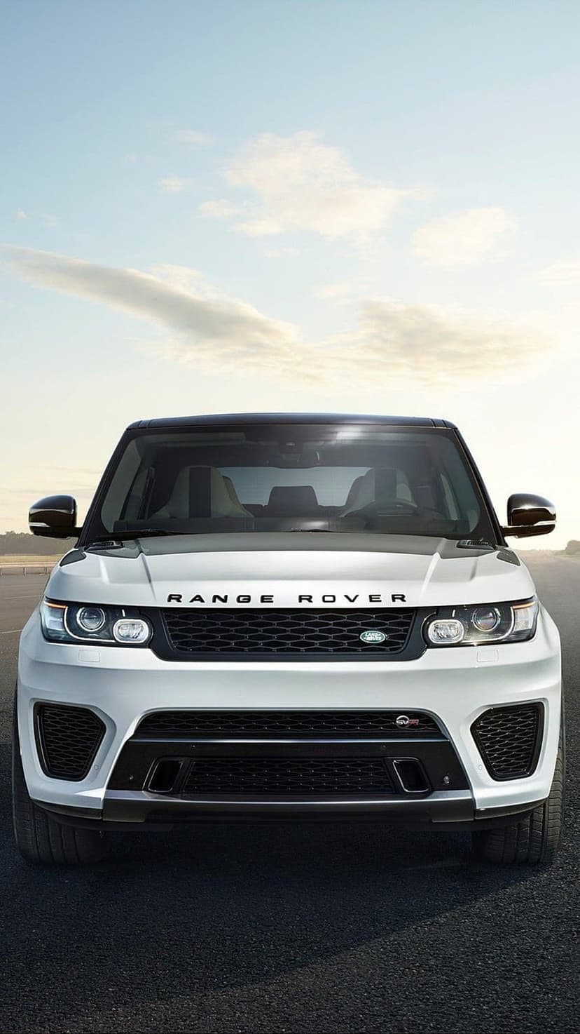 White Range Rover Sport SUV parked on a dark asphalt road under a clear blue sky with light clouds in front view.