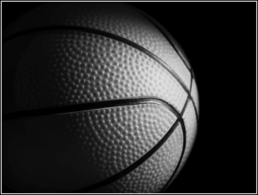 Basketball surface with pebbled leather texture and curved black seams under high-contrast studio lighting.