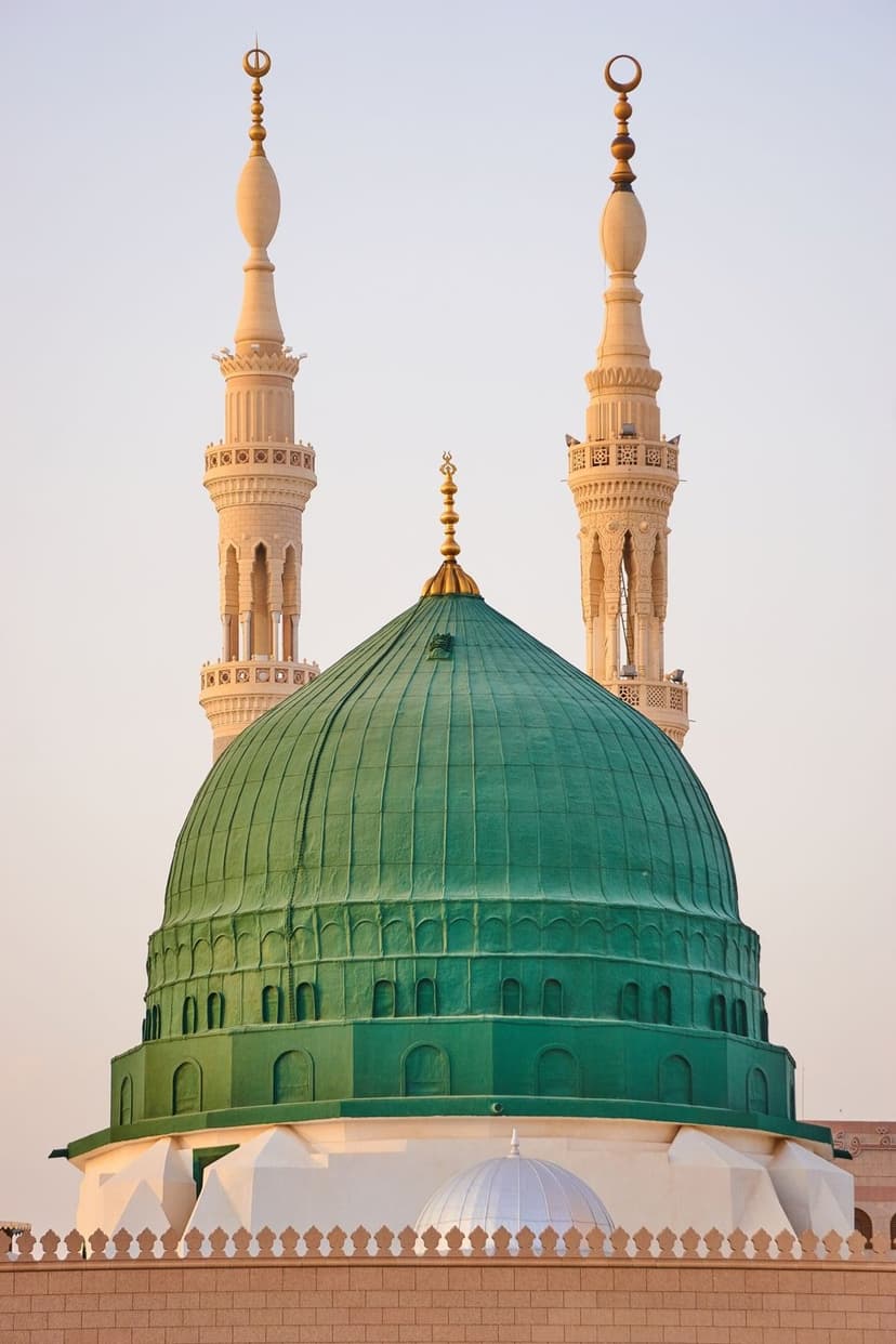 The vibrant Green Dome of the Prophet's Mosque sits beside towering white minarets under a bright morning sky.
