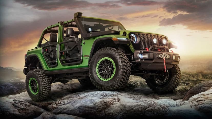 Green Jeep Wrangler with tube doors and off-road tires parked on grey rocks during a vibrant golden hour sunset.