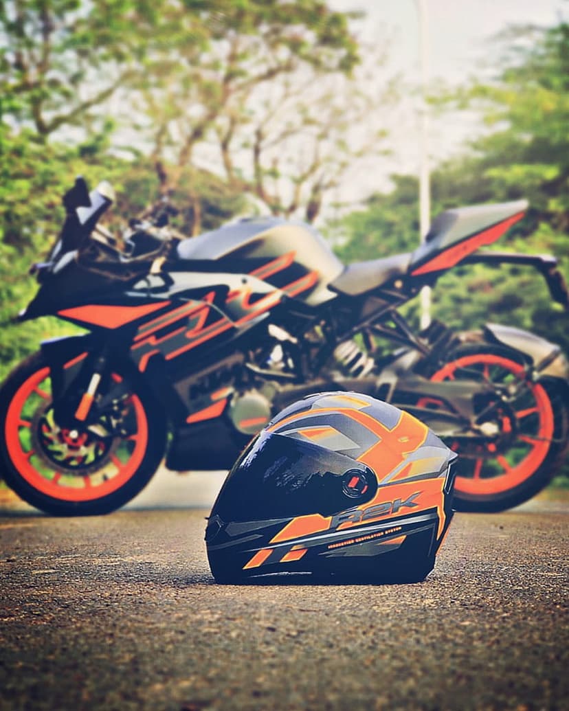 KTM sports bike with orange accents parked behind a matching full-face helmet on a gray asphalt road surface.