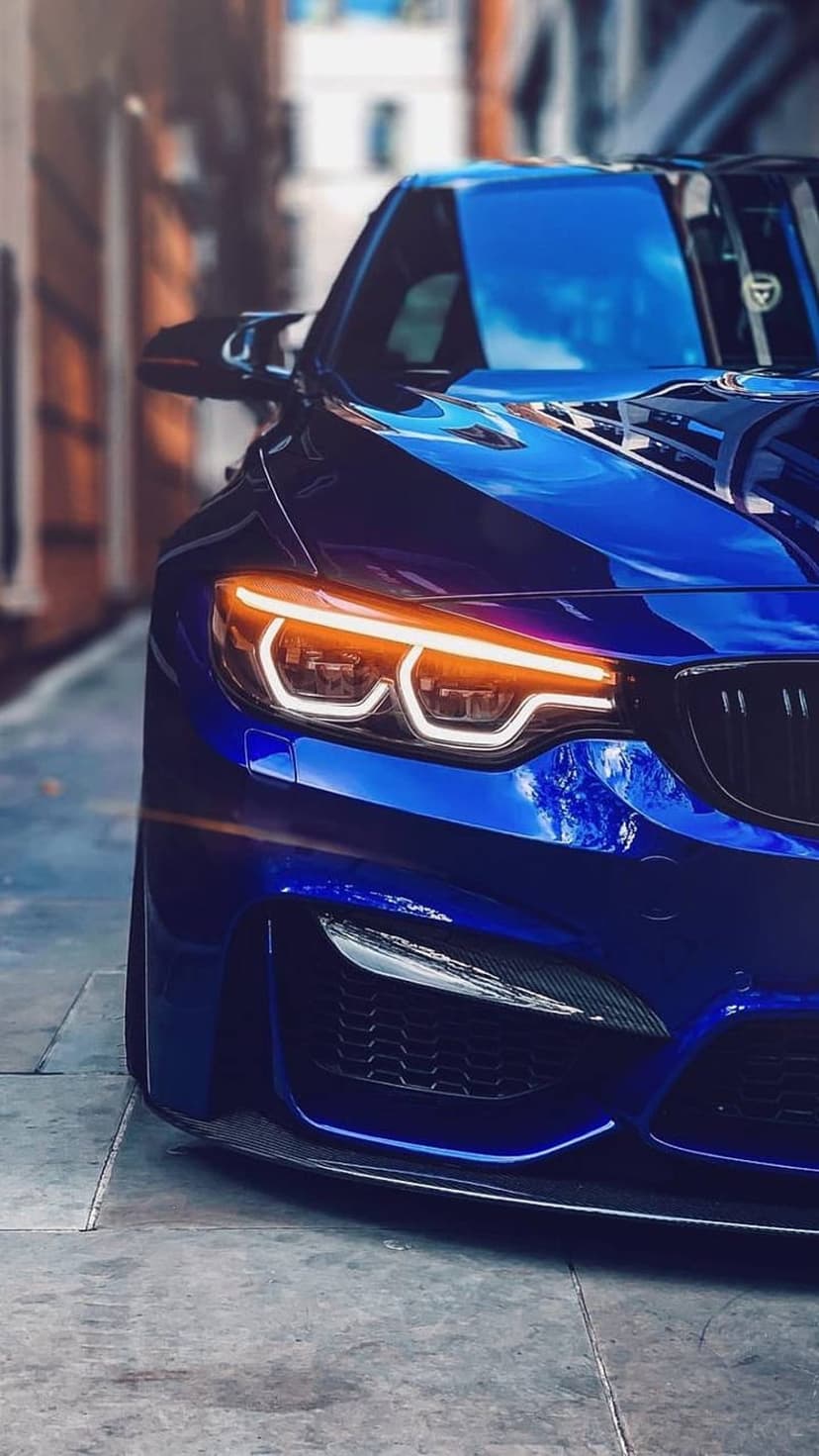 BMW M4 front headlights and kidney grille glowing with orange light on a dark textured city street at night.