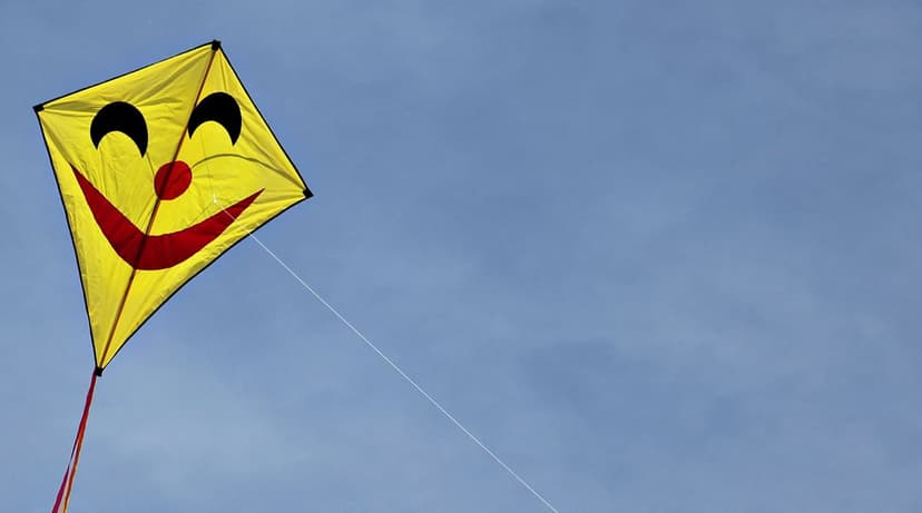 Yellow smiley face kite with a red grin soaring through a clear blue sky on a thin diagonal string tether.