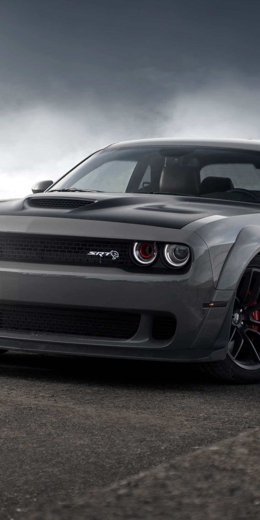 Dodge Challenger SRT Hellcat with widebody fenders and red air intake headlights against a cloudy sky.