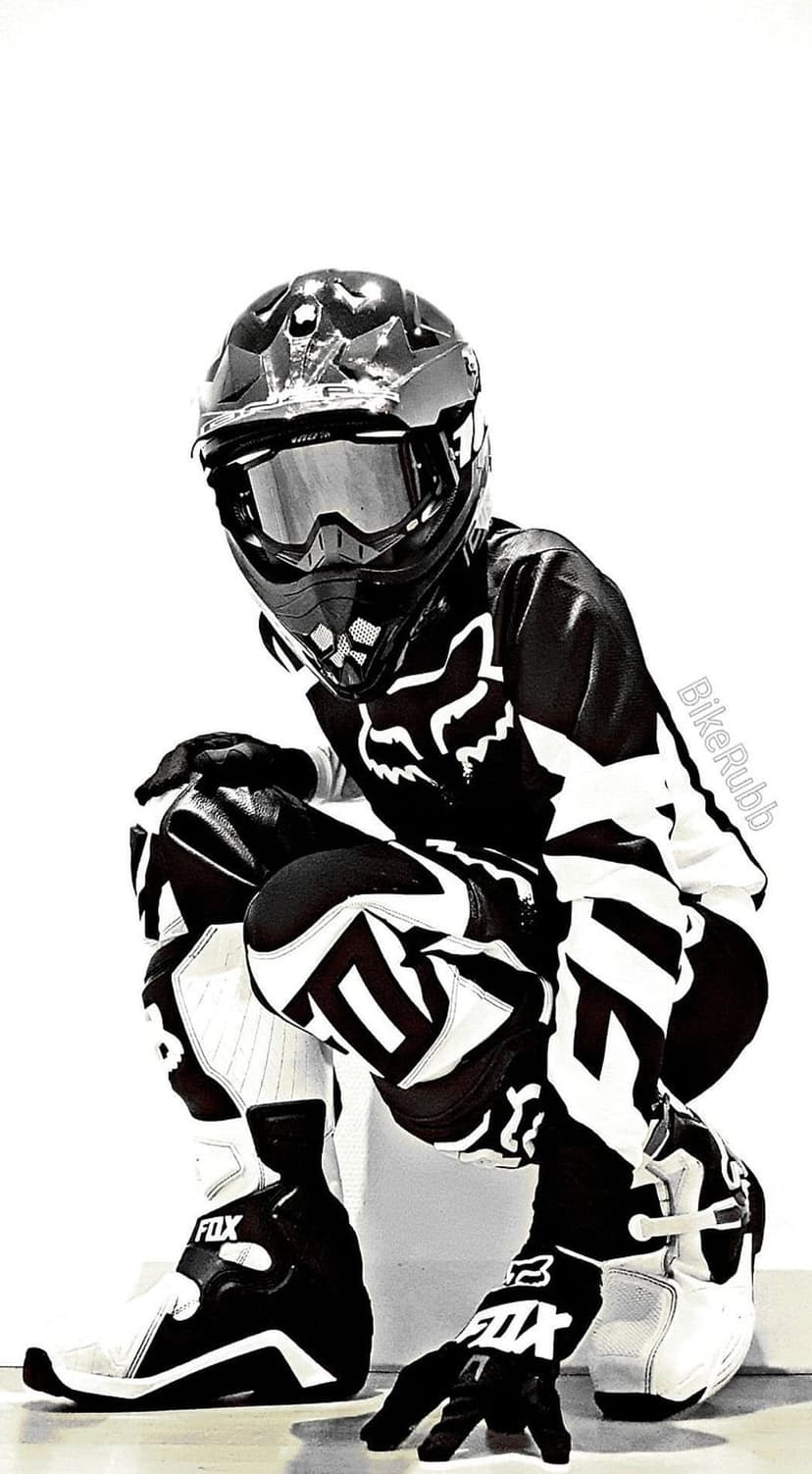 Motocross rider in full protective gear crouches low in a high-contrast black and white vertical sports portrait.