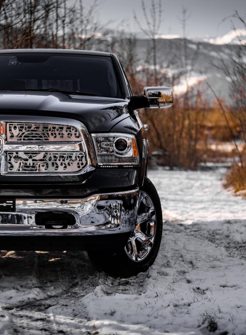 Black pickup truck with custom chrome grille on a snowy path with a blurred winter forest background.