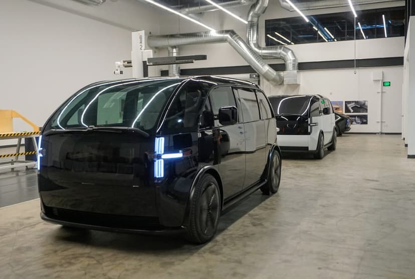 Black Canoo electric van in a modern industrial studio with white LED headlights and sleek reflective body.