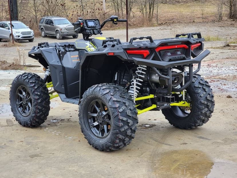 Black Polaris Sportsman ATV with neon yellow suspension and aggressive off-road tires in an outdoor lot.
