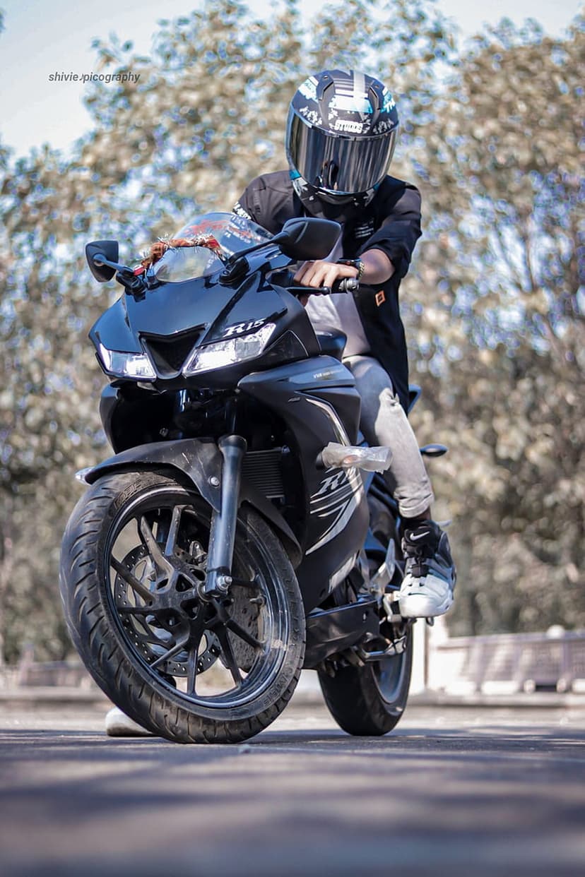 Biker wearing a black helmet and jacket on a sportbike with sharp lines against a soft bokeh forest background.