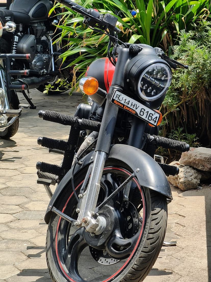 Royal Enfield motorcycle featuring a circular LED headlight, black fuel tank with red stripe, and textured grips.