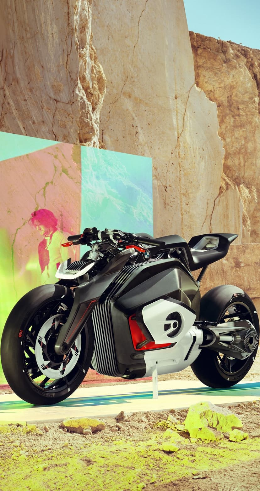 BMW electric motorcycle concept with white bodywork parked near rocky formations and colorful abstract murals.