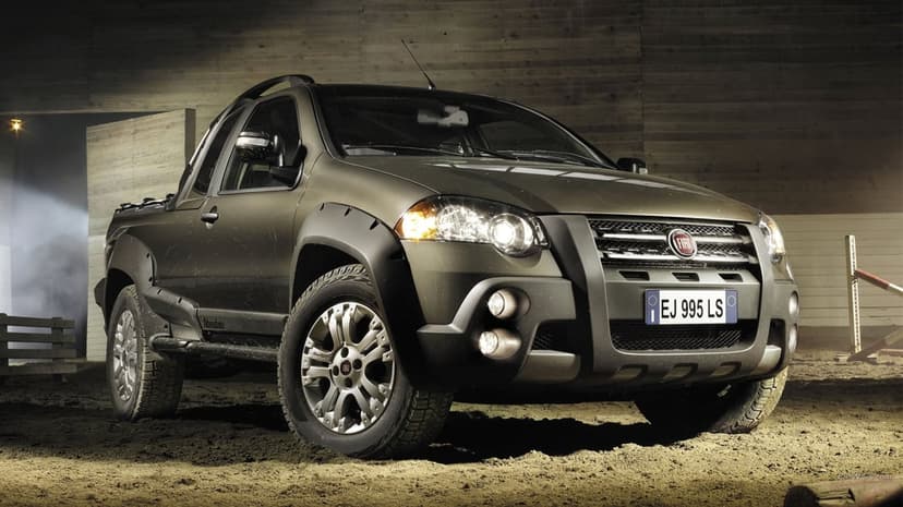 Metallic olive Fiat Strada Adventure truck on a sandy floor with dramatic lighting and wooden background.