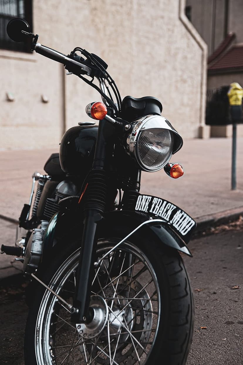 Black motorcycle with spoked wheels and a license plate reading ONE TRACK MIND parked by a stone wall.