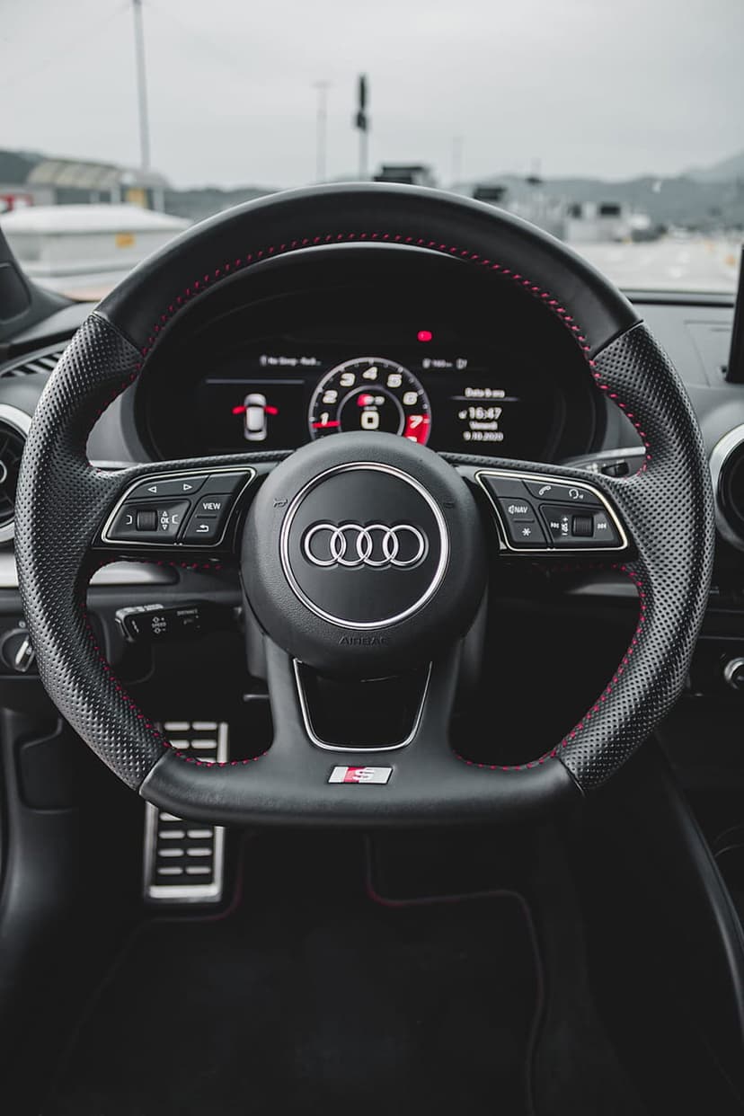 Audi RS steering wheel featuring red stitching and a digital dashboard inside a modern luxury vehicle cockpit.