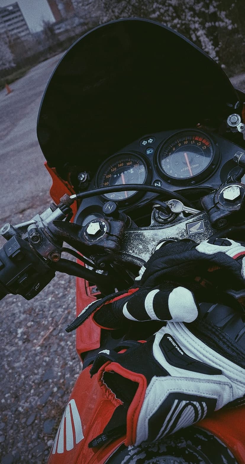 Racing gloves and dual motorcycle gauges sit atop a red sportbike cockpit with an ignition key inserted.