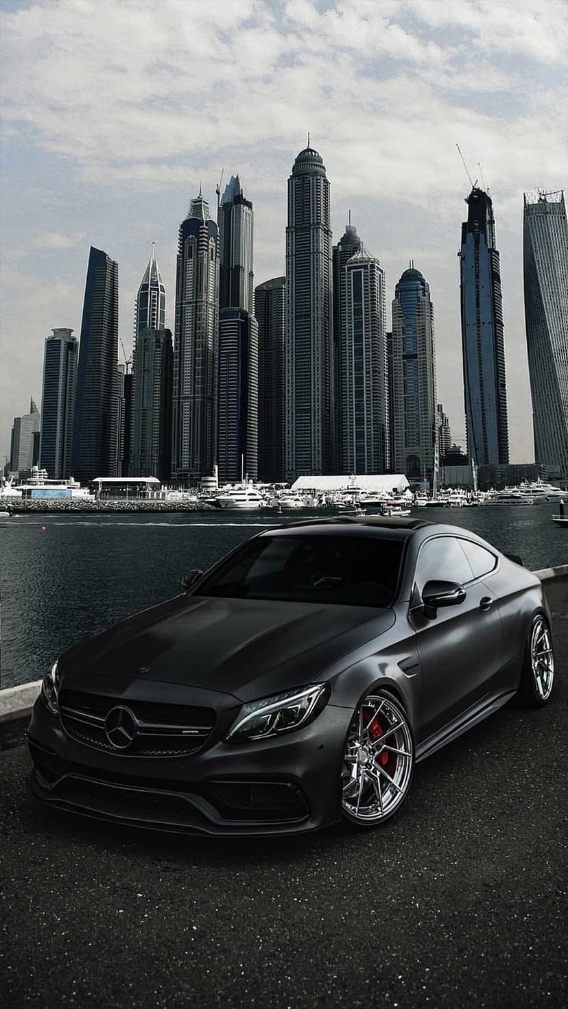 Matte black Mercedes-AMG C63 Coupe parked by the Dubai Marina waterfront with tall skyscrapers in the background.