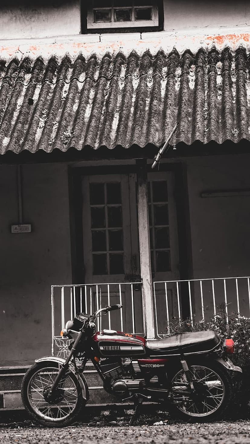 Yamaha RX100 motorcycle in dark red parked before a weathered building with corrugated metal and wooden doors.