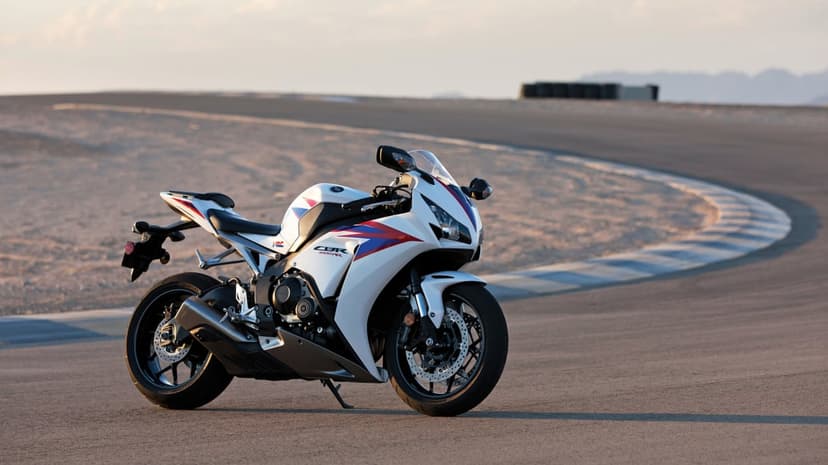 White Honda CBR1000RR motorcycle with red and blue accents parked on an asphalt racetrack at sunset.