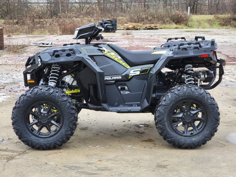 Side profile of a black Polaris Sportsman 850 ATV with lime yellow accents on a rugged gravel lot background.