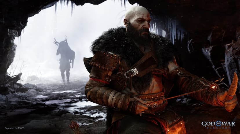 Kratos sits in a dark cave by a fire as Atreus returns with a hunt in a snowy landscape beyond the entrance.