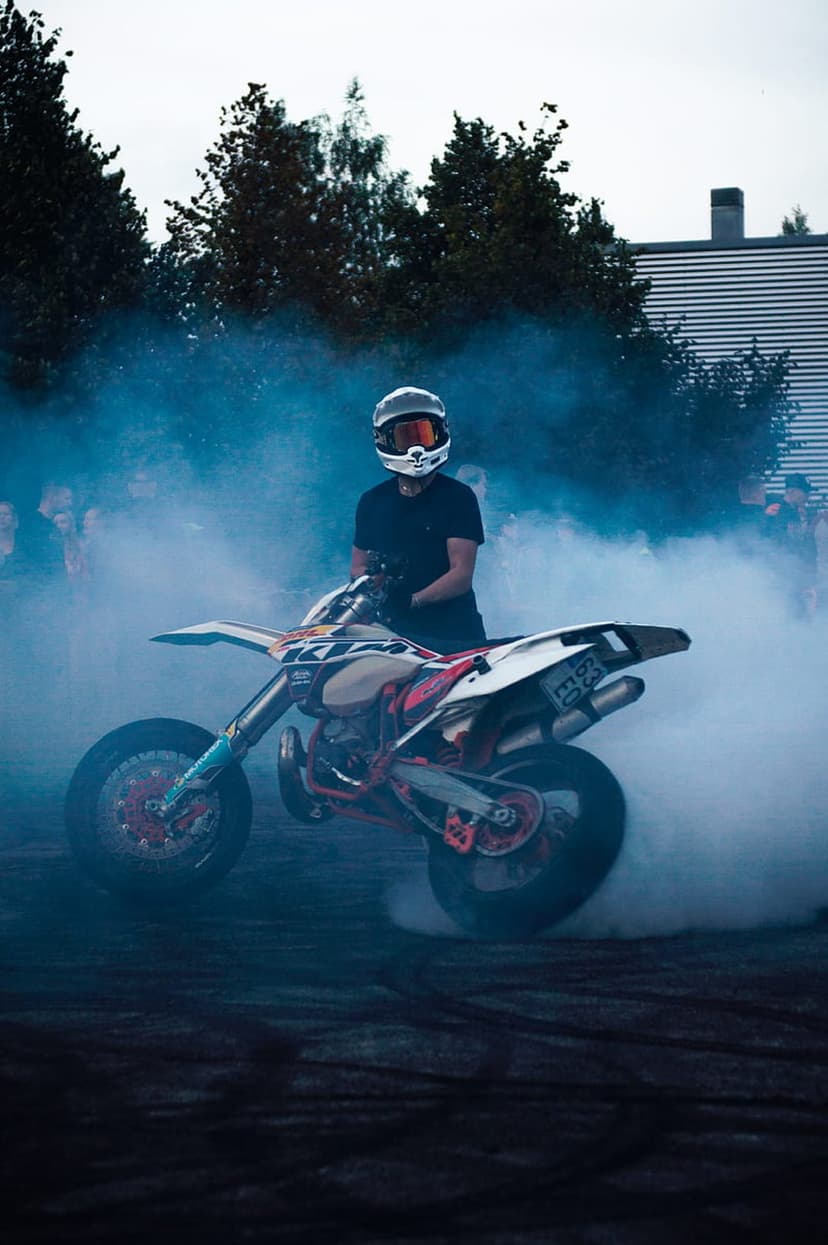Motorcyclist wearing a helmet performs a burnout while surrounded by a thick cloud of vibrant blue smoke plumes.