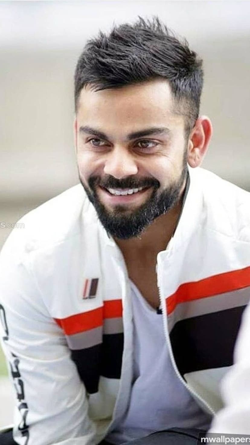 Virat Kohli smiling in a white jacket with orange accents, featuring his signature beard and stylish hairstyle.