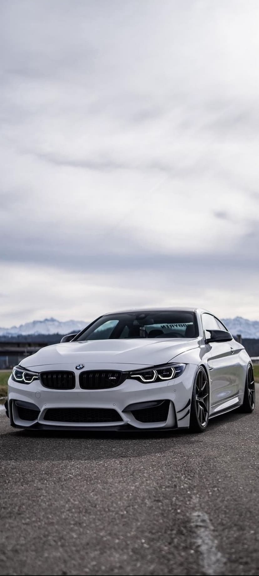 White BMW M4 Coupe parked on asphalt with hazy mountains and a cloudy sky in the background of the car.