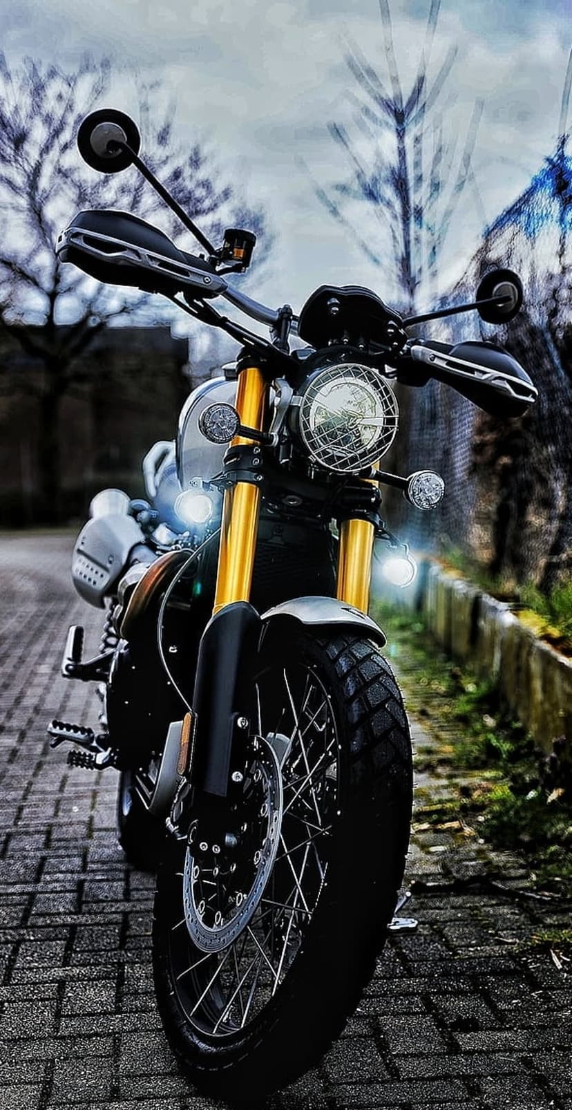 Retro motorcycle with golden forks and round headlights sits on a textured cobblestone street under soft light.