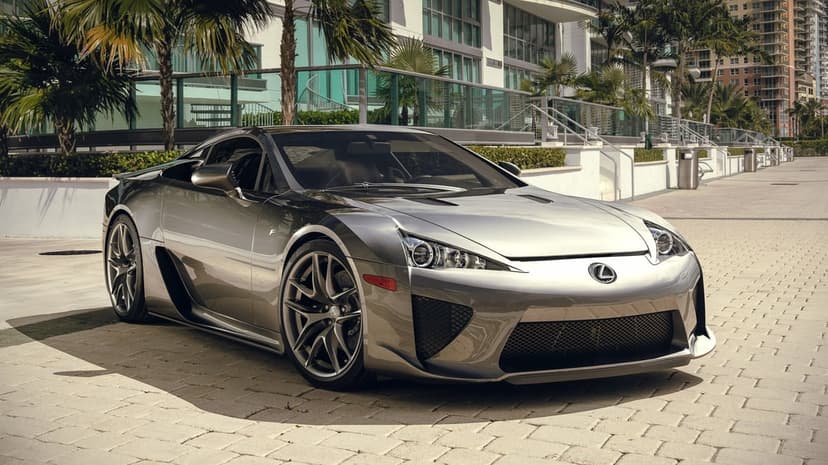 Lexus LFA supercar in silver parked on a stone walkway with palm trees and modern glass buildings.