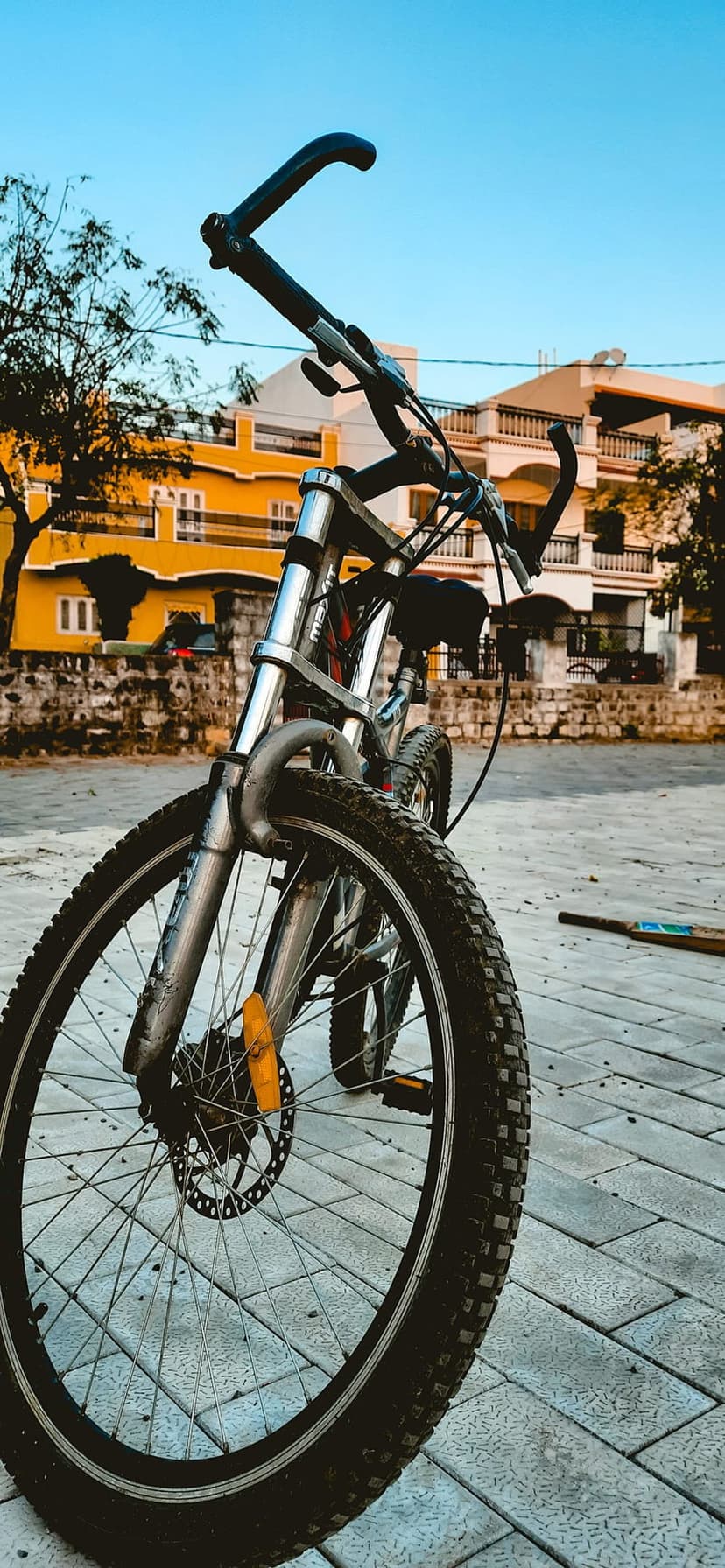Bicycle front wheel and handlebars parked near a textured stone wall and a bright yellow multi-story building.