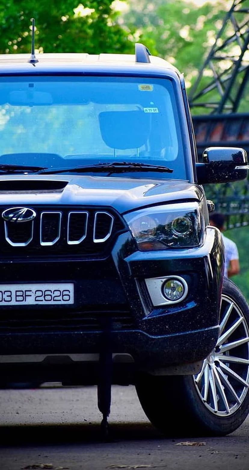 Black Mahindra Scorpio SUV front view featuring a chrome-accented grille, headlights, and green blurred background.