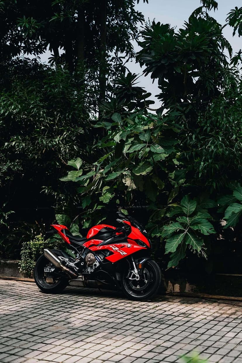 Red sport motorcycle parked on a stone walkway surrounded by dense green trees and vibrant forest foliage.