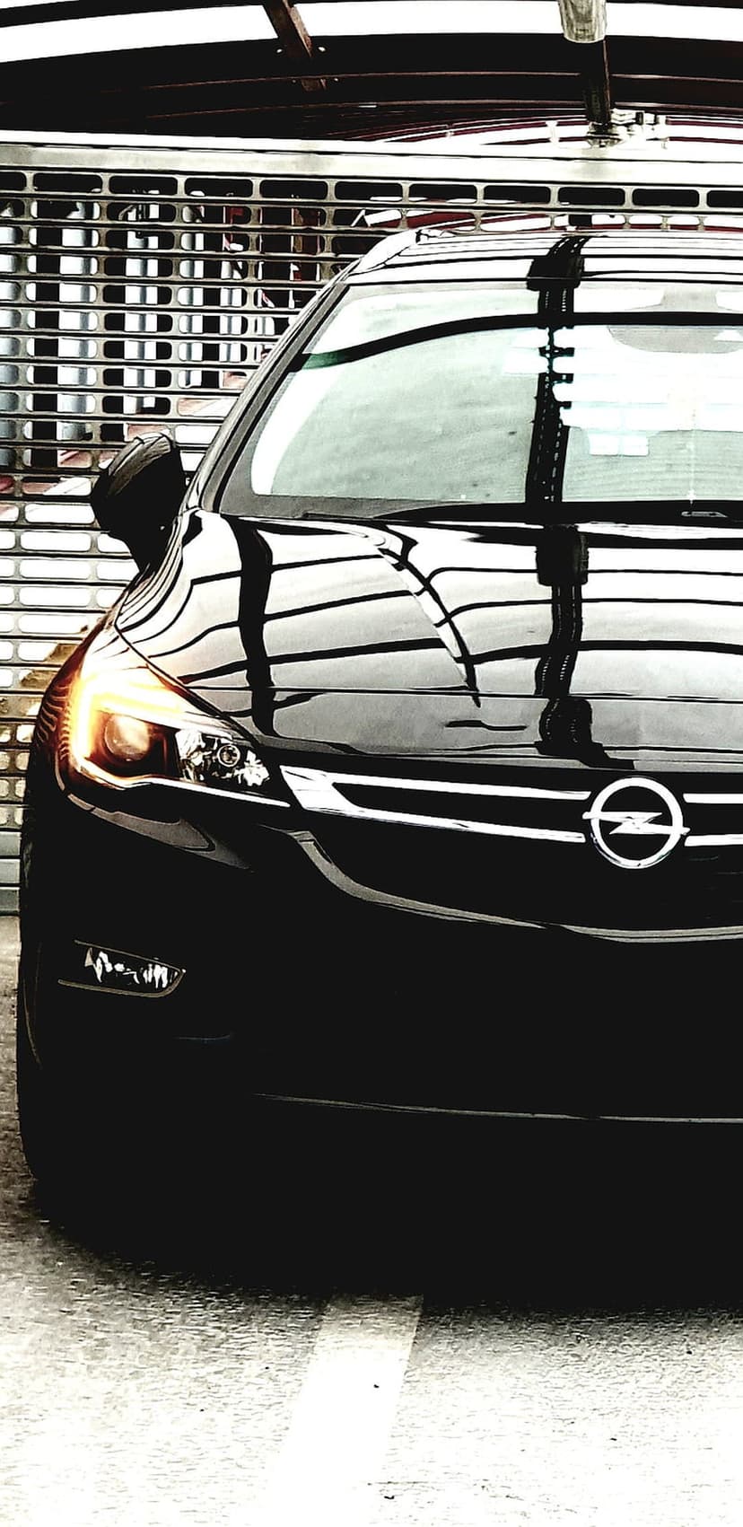 Black Opel Astra front grille with an illuminated orange headlight and chrome logo against a metal shutter.