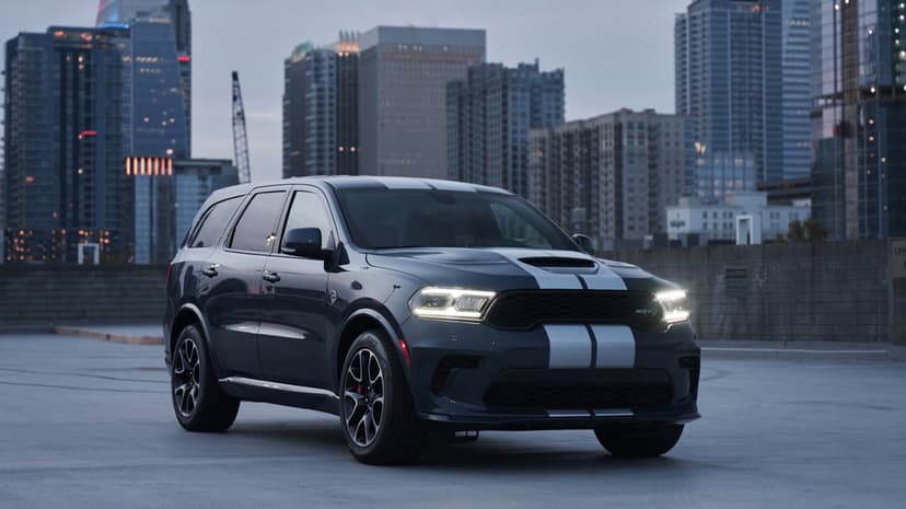 Dodge Durango SRT Hellcat parked on a rooftop with white racing stripes and a glowing city skyline at dusk.