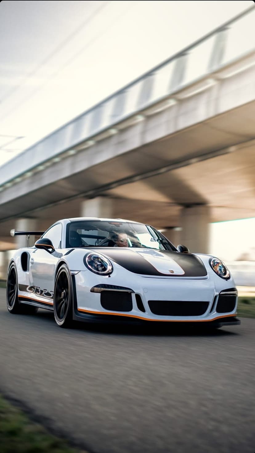 White Porsche 911 GT3 RS with racing stripes drives under a blurred bridge in a vertical car phone background.