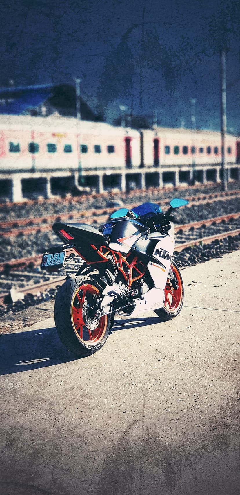 Orange KTM motorcycle parked on gravel beside a speeding train under a dark twilight sky at dusk.