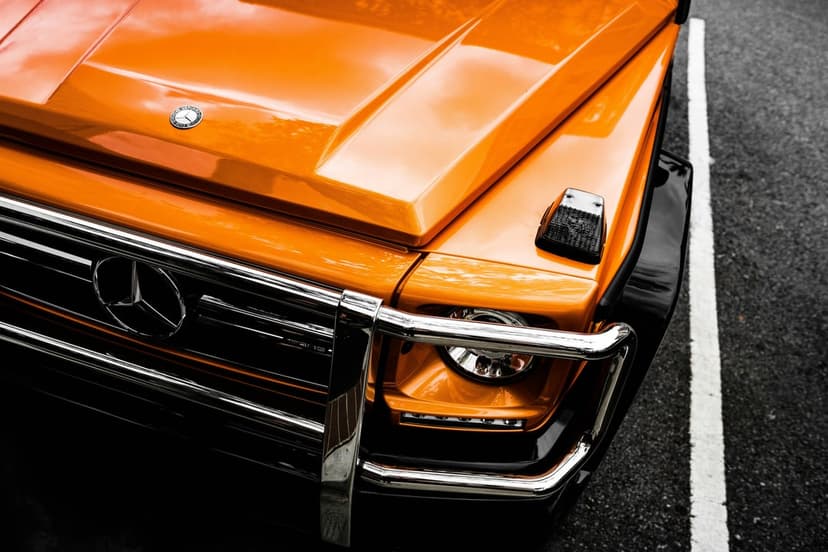 Orange Mercedes-Benz G-Wagen front grille, circular headlight, and chrome bumper on a textured asphalt surface.