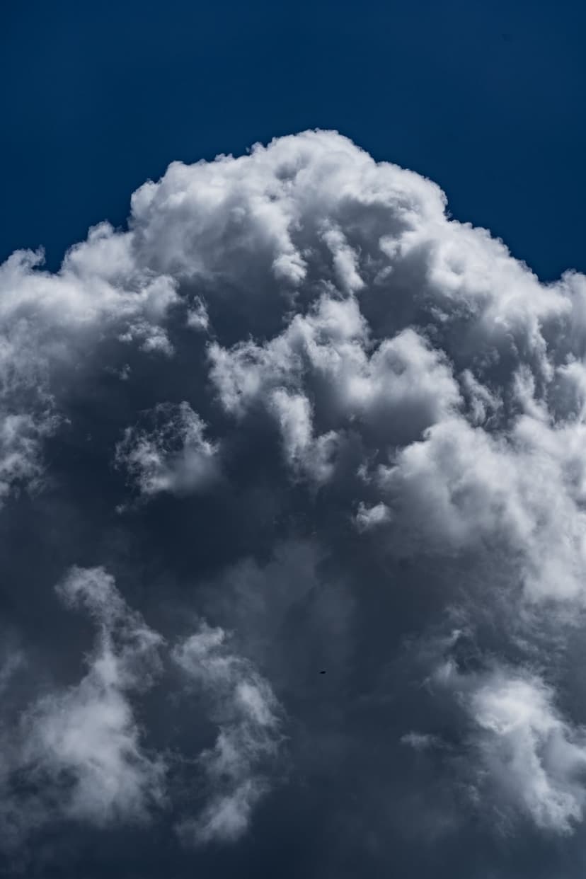Towering white thunderhead cloud with textured vapor and soft shadows against a deep blue atmosphere.