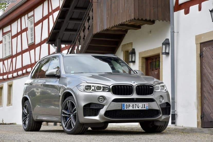 Silver BMW X5 M SUV parked on gravel in front of a traditional German half-timbered house with wooden stairs.