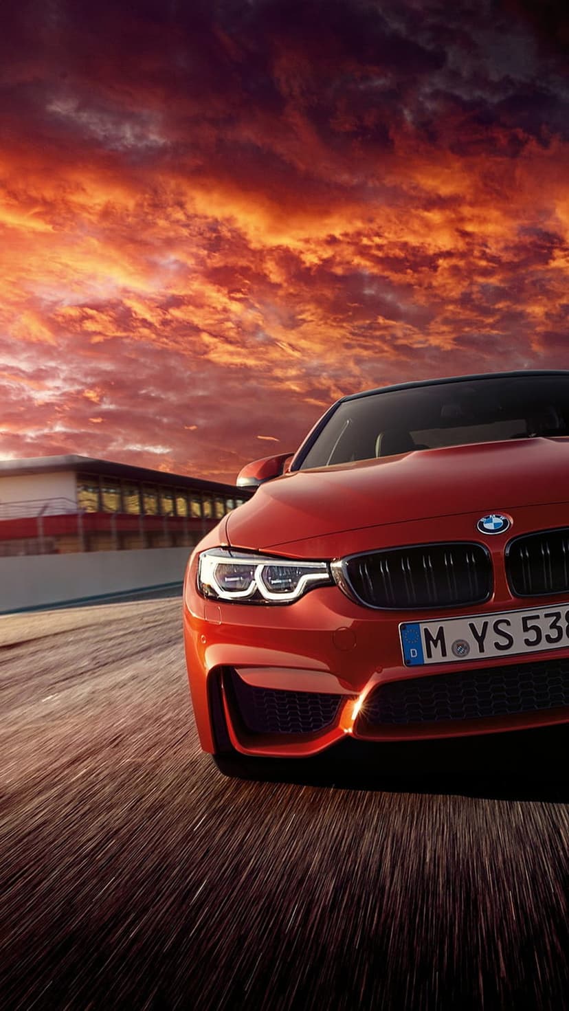 Red BMW M4 driving fast on a racetrack under a fiery orange sunset sky with cinematic motion blur on the road.