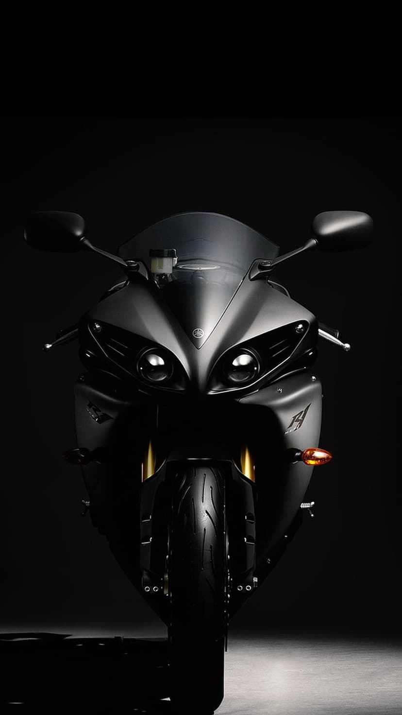 Yamaha R1 motorcycle in matte black with dual headlights facing forward inside a dimly lit photography studio.